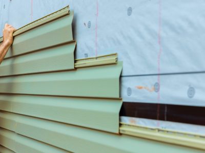 Construction worker carefully lays green siding on building exterior while ensuring proper fit.